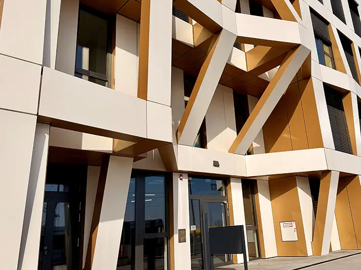 Detailaanzicht van de entree van Brainfactory Bochum met een opvallende gevelstructuur, schuine ondersteuningselementen en moderne architectuur in wit- en goudtinten.