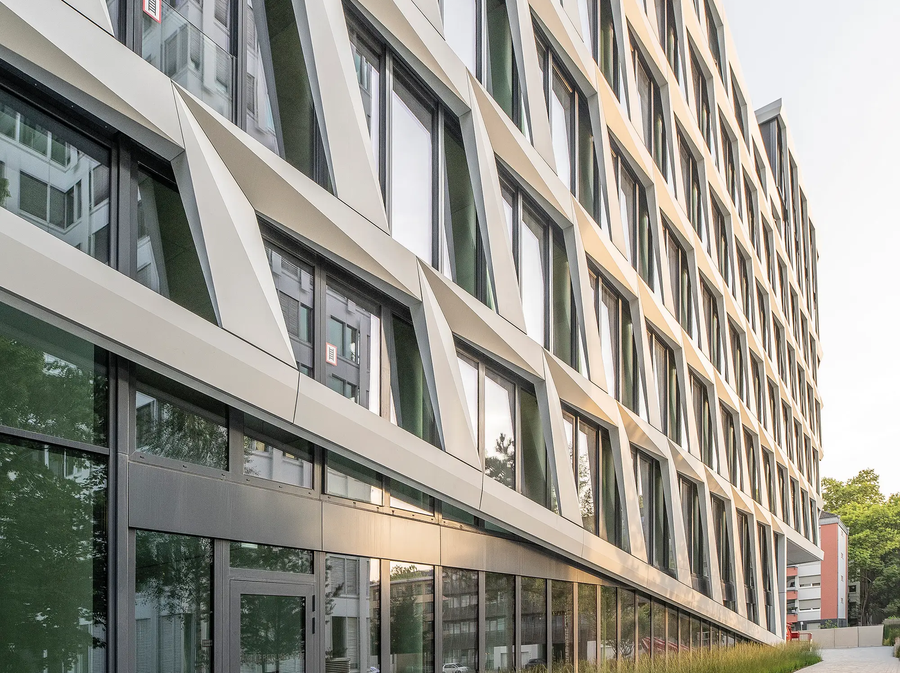 Zijaanzicht van het ONE PLAZA-gebouw met een gestructureerde gevel, grote ramen en een beplante voortuin.